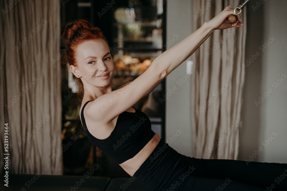 Young ginger female smiling while doing exercises on pilates reformer Young ginger female smiling while doing exercises on pilates reformer