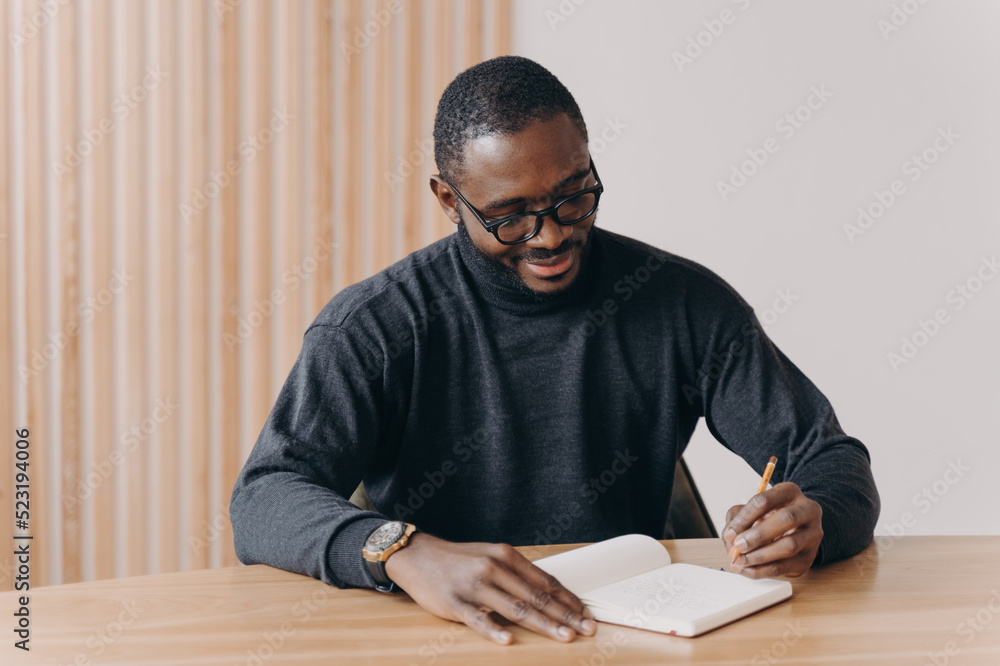 Young african american man entrepreneur in glasses taking notes in agenda Young african american man entrepreneur in glasses taking notes in agenda
