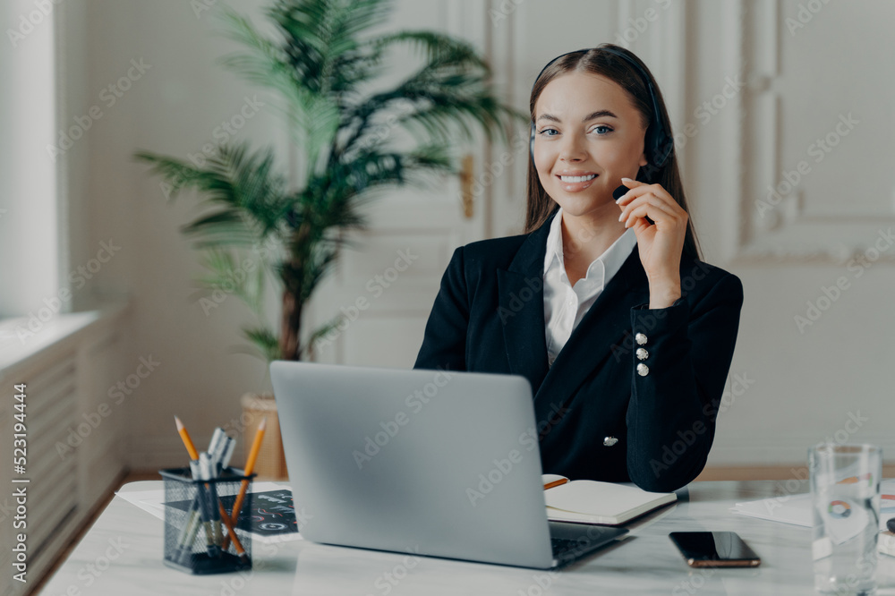 Female office worker in headset smiling at camera during online meeting Female office worker in headset smiling at camera during online meeting