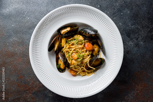 pasta spaghetti with mussels and tomatoes on white plate on dark stone table top view