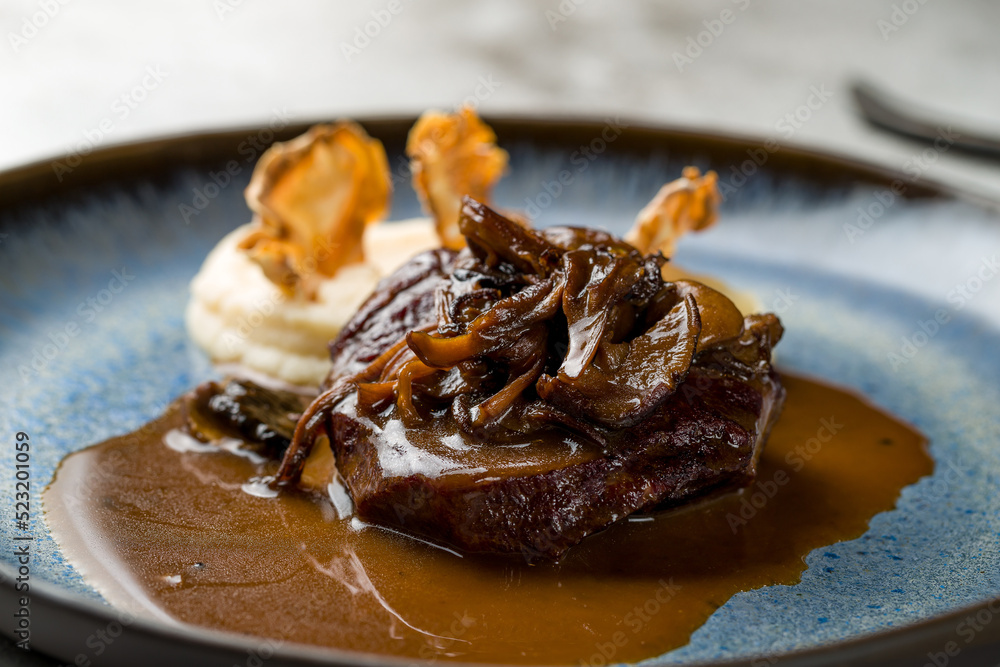 Beef cheeks with mashed potatoes and mushrooms on demiglass sauce on grey table macro close up