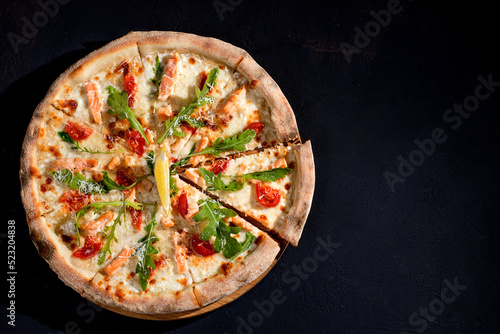 Pizza with salmon, mozzarella, cherry tomatoes, arugula, lemon and parmesan. Italian cuisine. On a black background. Free space for text. View from above.