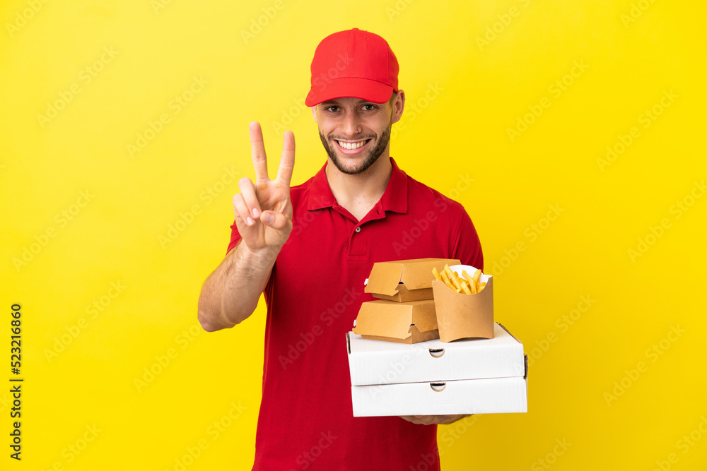 pizza delivery man picking up pizza boxes and burgers over isolated background smiling and showing victory sign pizza delivery man picking up pizza boxes and burgers over isolated background smiling and showing victory sign