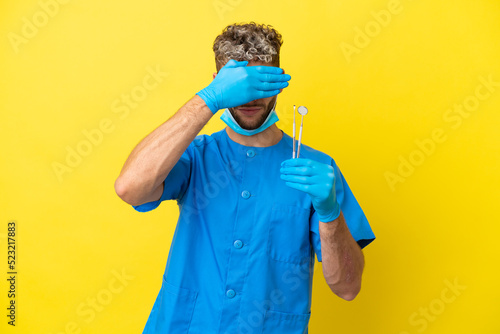Dentist caucasian man holding tools isolated on yellow background covering eyes by hands. Do not want to see something