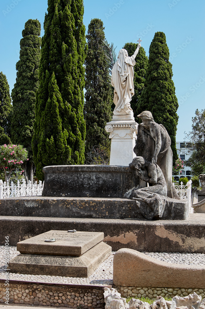 Partial view of the Sitges cemetery with richly ornamented pantheons and niches in the background, as well as some very leafy trees under the blue sky for All Souls' Day, All Saints' Day and Halloween