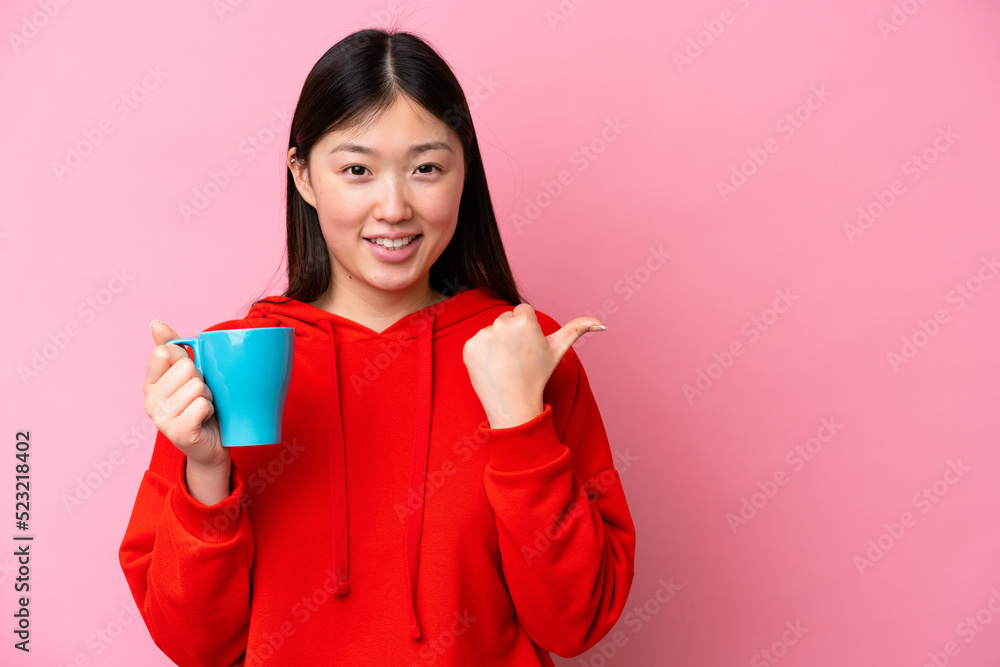 Young Chinese woman holding cup of coffee isolated on pink background pointing to the side to present a product Young Chinese woman holding cup of coffee isolated on pink background pointing to the side to present a product