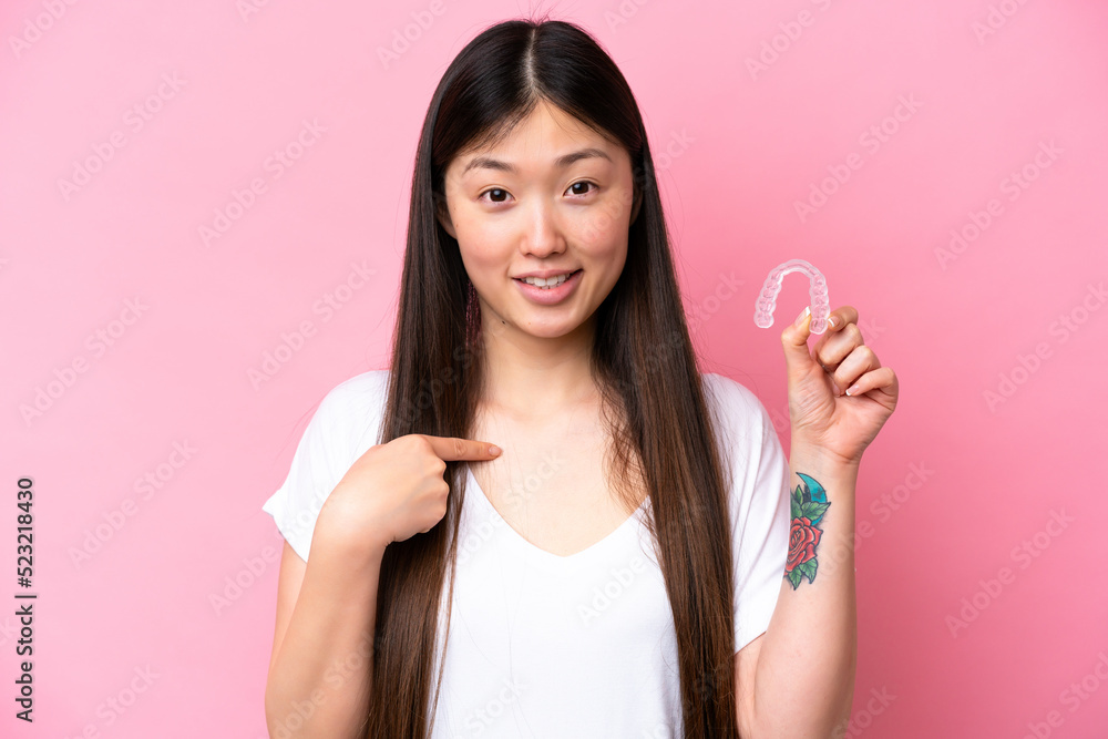 Young Chinese woman holding invisible braces isolated on pink background with surprise facial expression Young Chinese woman holding invisible braces isolated on pink background with surprise facial expression