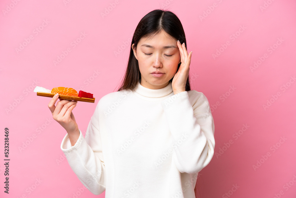 Young Chinese woman holding sashimi isolated on pink background with headache Young Chinese woman holding sashimi isolated on pink background with headache