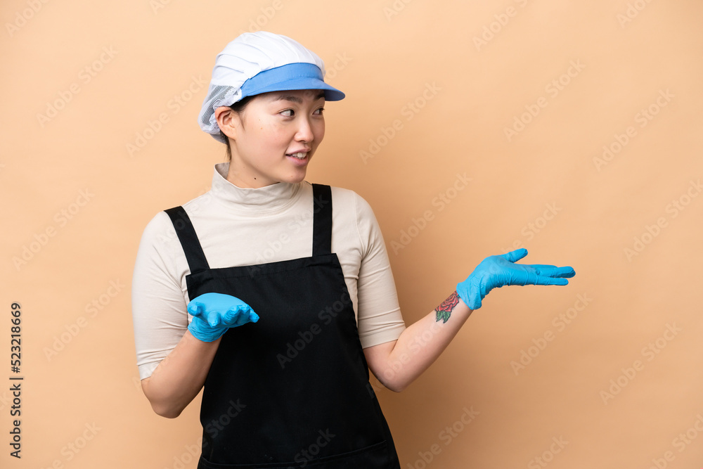 Young Chinese Fishmonger woman wearing an apron and holding a raw fish isolated on pink background with surprise expression while looking side Young Chinese Fishmonger woman wearing an apron and holding a raw fish isolated on pink background with surprise expression while looking side
