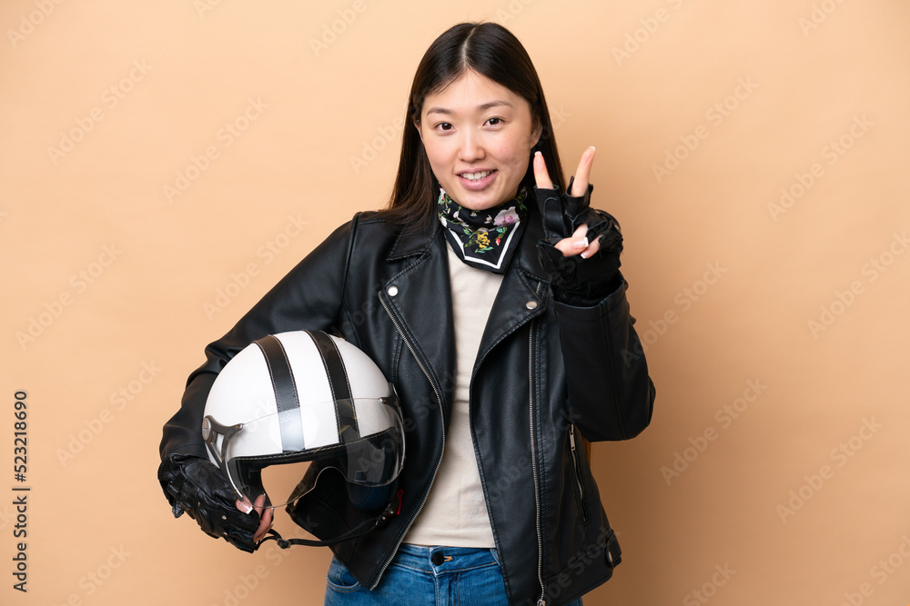 Young Chinese woman with a motorcycle helmet isolated on beige background smiling and showing victory sign