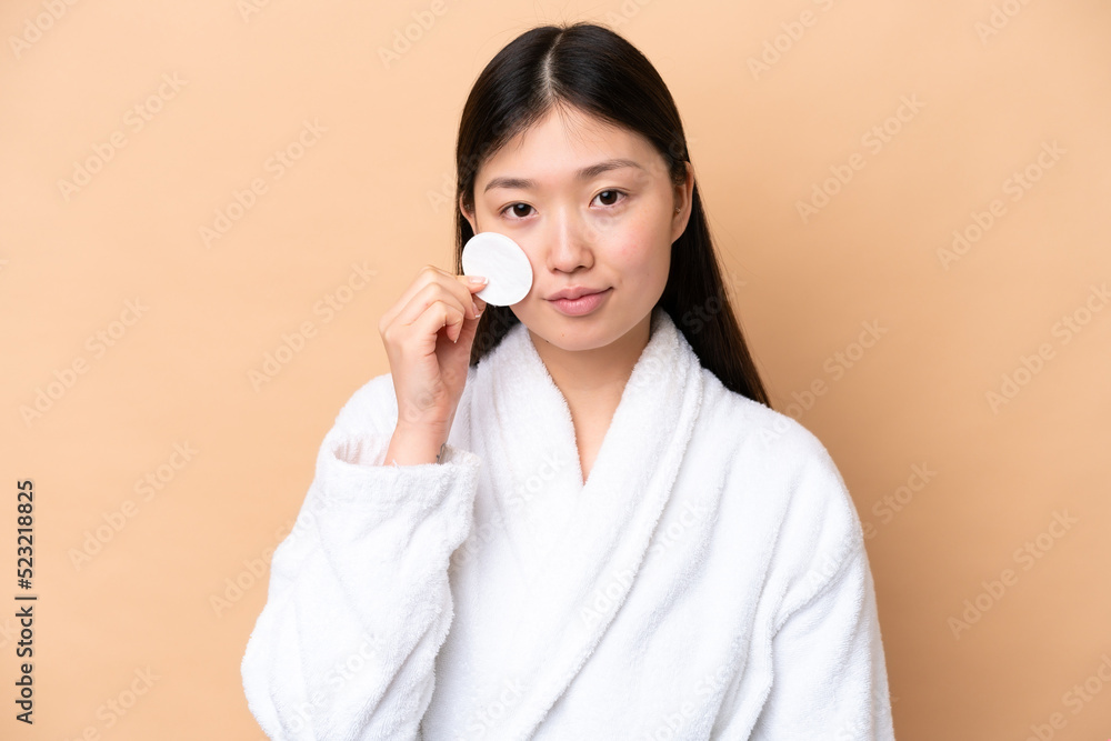 Young Chinese woman isolated on beige background with cotton pad for removing makeup from her face Young Chinese woman isolated on beige background with cotton pad for removing makeup from her face