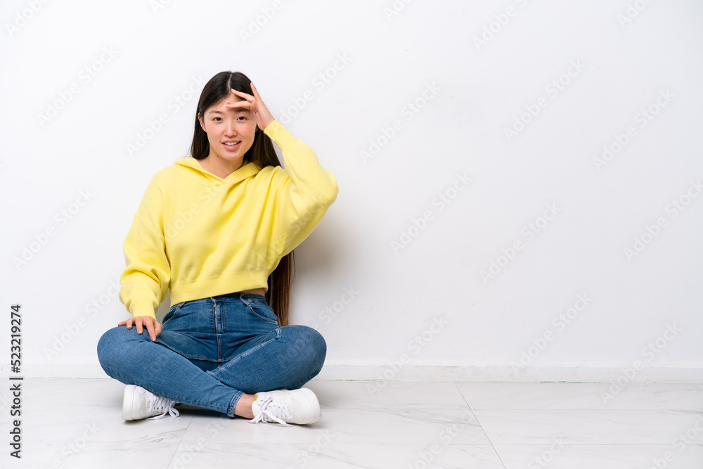 Young Chinese woman sitting on the floor isolated on white wall looking far away with hand to look something Young Chinese woman sitting on the floor isolated on white wall looking far away with hand to look something
