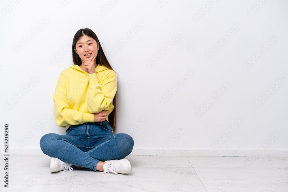 Young Chinese woman sitting on the floor isolated on white wall smiling Young Chinese woman sitting on the floor isolated on white wall smiling