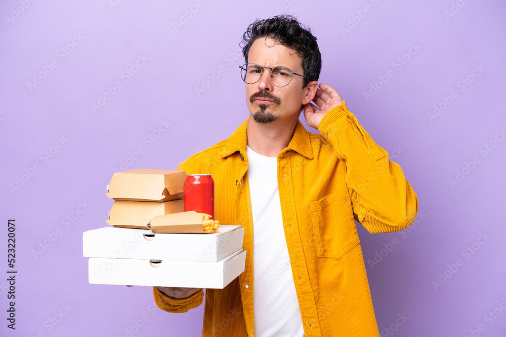Young caucasian man holding fast food isolated on purple background having doubts Young caucasian man holding fast food isolated on purple background having doubts