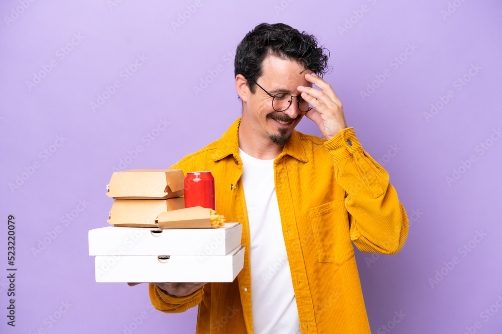 Young caucasian man holding fast food isolated on purple background laughing Young caucasian man holding fast food isolated on purple background laughing