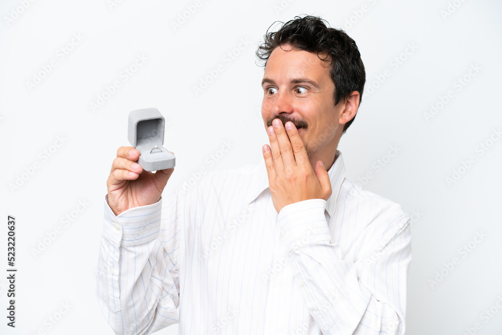 Young man holding a engagement ring isolated on white background with surprise and shocked facial expression Young man holding a engagement ring isolated on white background with surprise and shocked facial expression