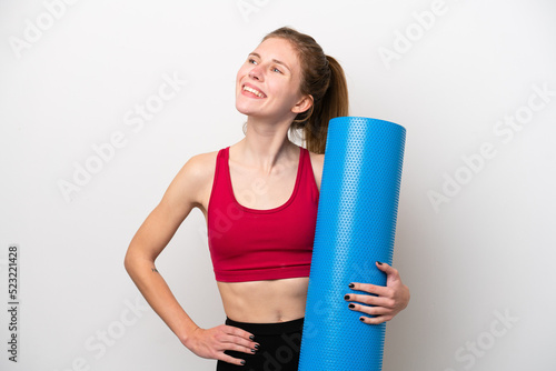 Young sport English woman going to yoga classes while holding a mat isolated on white background posing with arms at hip and smiling