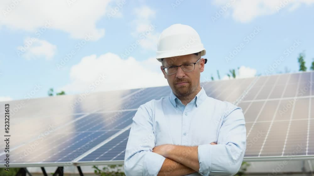 Portrait of confident engineer of solar cell farm industry. Staff confident pose Solar cell panel installation. Close up portrait of male worker in protective helmet standing near solar panel Portrait of confident engineer of solar cell farm industry. Staff confident pose Solar cell panel installation. Close up portrait of male worker in protective helmet standing near solar panel