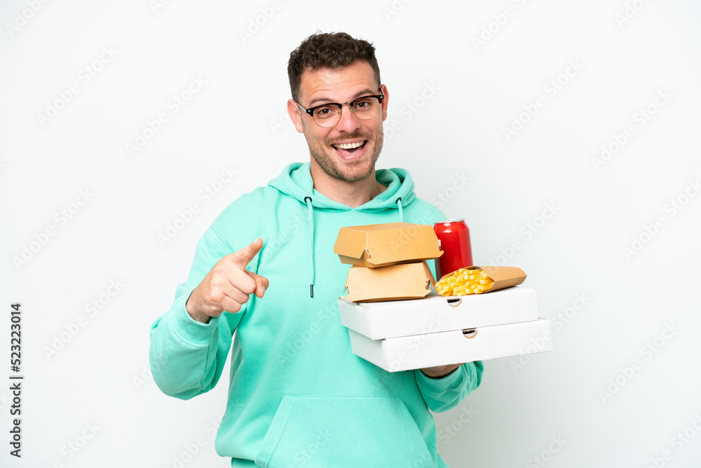 Young caucasian man holding fast food isolated on white background surprised and pointing front Young caucasian man holding fast food isolated on white background surprised and pointing front