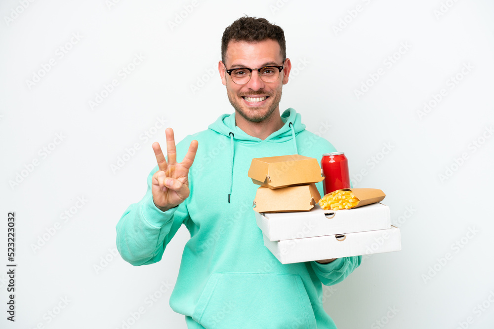 Young caucasian man holding fast food isolated on white background happy and counting three with fingers Young caucasian man holding fast food isolated on white background happy and counting three with fingers