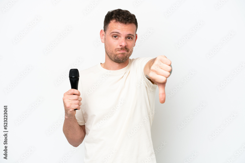 Young caucasian singer man picking up a microphone isolated on white background showing thumb down with negative expression Young caucasian singer man picking up a microphone isolated on white background showing thumb down with negative expression