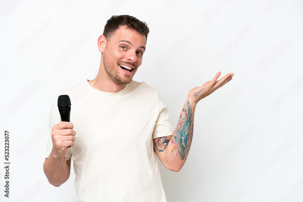 Young caucasian singer man picking up a microphone isolated on white background extending hands to the side for inviting to come Young caucasian singer man picking up a microphone isolated on white background extending hands to the side for inviting to come