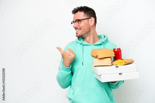 Young caucasian man holding fast food isolated on white background pointing to the side to present a product