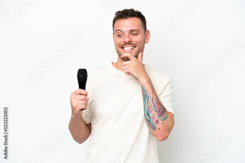 Young caucasian singer man picking up a microphone isolated on white background looking to the side and smiling