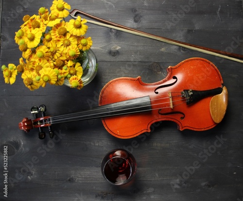 violin  bow  yellow flowers boquet and glass of cognac on black wooden background