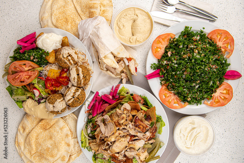 Middle eastern or arabic dishes and assorted meze, white table background. falafel, chicken shawarma sandwich, chicken plate, hummus, tabbouleh, tabouli, Lebanese bread, Halal food. Lebanese cuisine