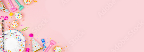 Birthday party corner border on a pastel pink banner background. Overhead view with cakes, party hats and confetti. Copy space. © Jenifoto