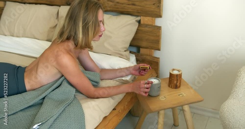 a blonde girl with a beautiful bare back lies on a bed and lights a candle on the bedside table with matches. woman lights a candle. blows on a match and puts out the fire. top view photo
