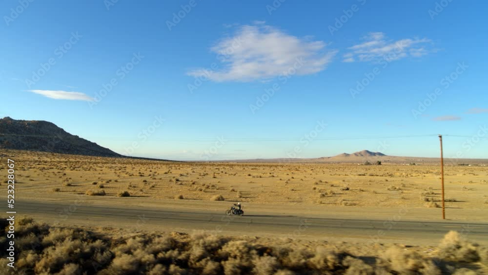 Aerial: Panning Shot Of Person Riding Motorbike On Desert Road, Drone Flying Forward Over Plants During Sunny Day - Mojave, California Aerial: Panning Shot Of Person Riding Motorbike On Desert Road, Drone Flying Forward Over Plants During Sunny Day - Mojave, California