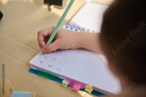 View from above with details on the hand of schoolchild, first grader holding a pencil and learning the writing, writes letters in a copybook. Education. Back to school. Knowledge concept, Copy space