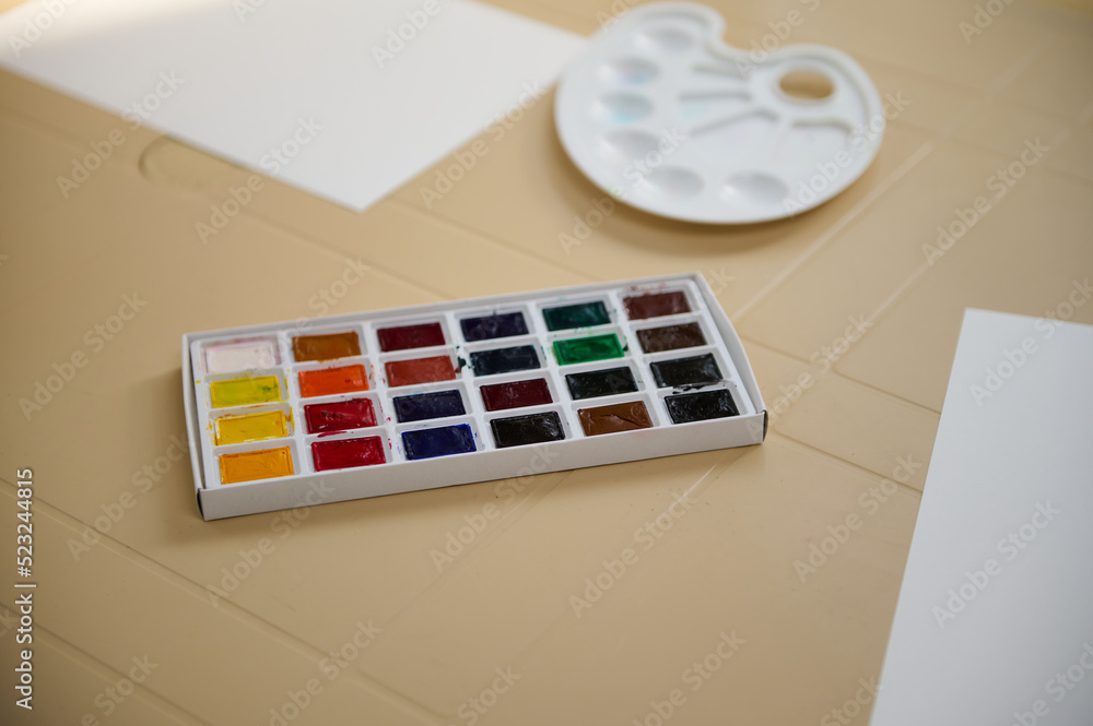 Directly above shot of a colorful palette with refills of watercolour paints and blank white paper sheet with copy space for advertising and promotional text. Painting and drawing activities. Directly above shot of a colorful palette with refills of watercolour paints and blank white paper sheet with copy space for advertising and promotional text. Painting and drawing activities.
