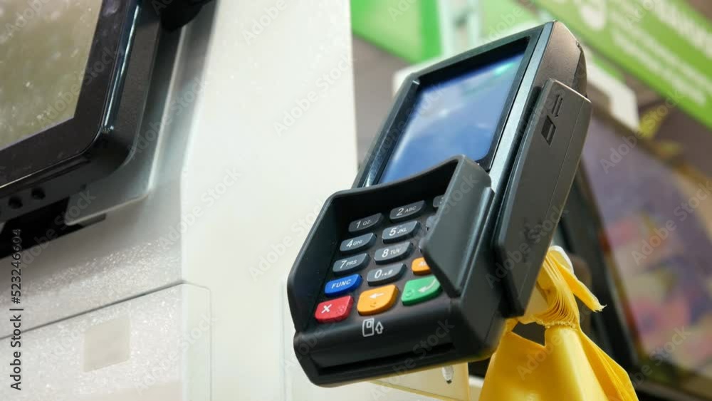 Close-up of a payment terminal at a self-service checkout and a male hand applies a credit card to it for payment Close-up of a payment terminal at a self-service checkout and a male hand applies a credit card to it for payment