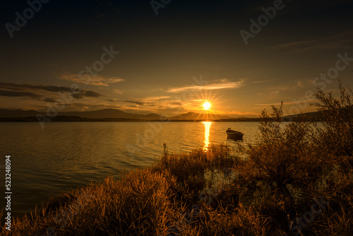 Krajobraz wodny. Widok na jezioro i zachód słońca. Piękny zachód słońca nad jeziorem ze starą łodzią i bezchmurnym niebem w tle, Polska 