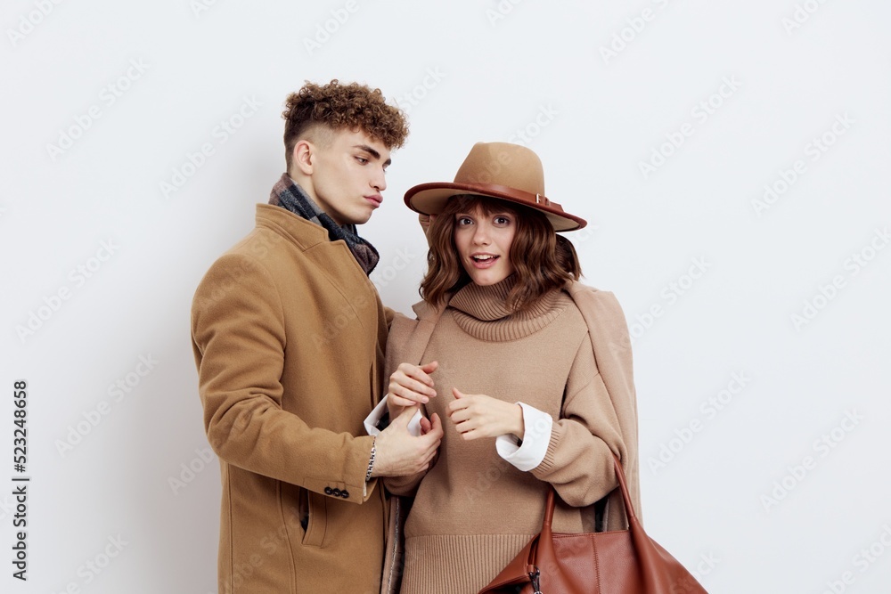 a cute couple is standing on a white background, wearing a coat. The man carefully adjusts the sleeve of the shirt of the woman standing next to him, who raised her hands up in embarrassment a cute couple is standing on a white background, wearing a coat. The man carefully adjusts the sleeve of the shirt of the woman standing next to him, who raised her hands up in embarrassment