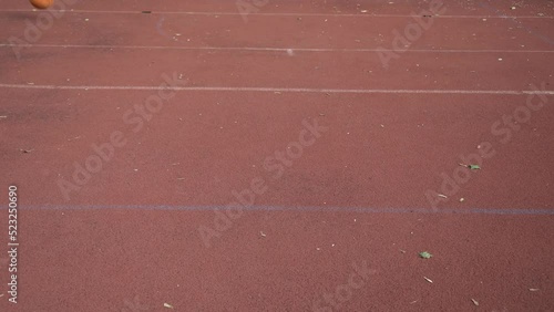 Basketball ball jumping through outdoor red street court by diagonal right to left
