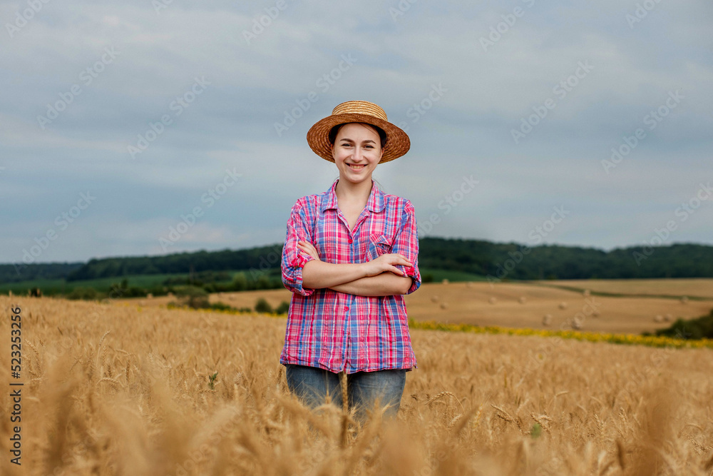 Obraz premium Young farmer woman in straw hat and checkered shirt on wheat ripe golden field. Agriculture. Wheat ripens
