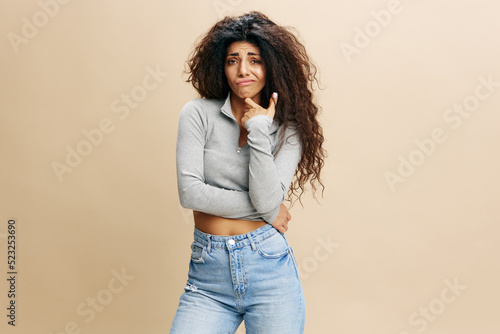 Portrait Of Pensive Latin Female Touching Chin And Looking To You With Doubt, Thoughtful Young Arab Woman Considering Interesting Offer While Standing Isolated Over Beige Background, Copy Space 