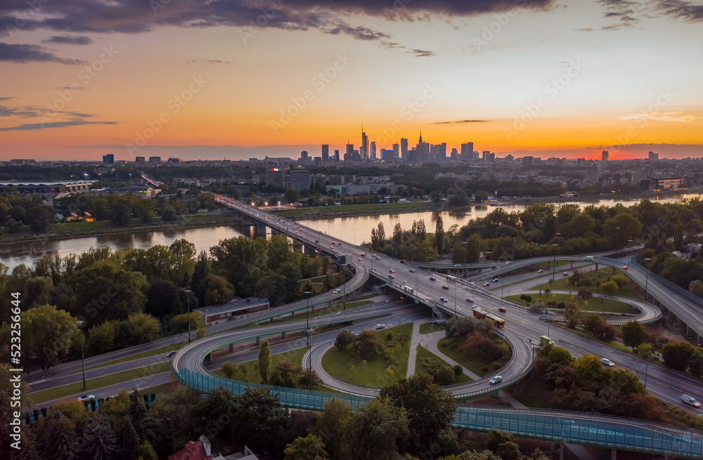 Stunning sunset skyline, aerial view Warsaw, Poland. Drone shot of city downtown business center skyscrapers in background. Highway bridge over river and driving cars, amazing cloudscape evening dusk