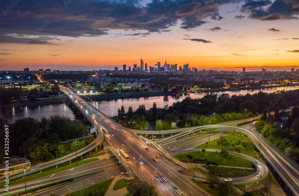Stunning sunset skyline, aerial view Warsaw, Poland. Drone shot of city downtown business center skyscrapers in background. Highway bridge over river and driving cars, amazing cloudscape evening dusk