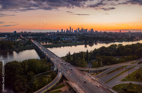 Stunning sunset skyline, aerial view Warsaw, Poland. Drone shot of city downtown business center skyscrapers in background. Highway bridge over river and driving cars, amazing cloudscape evening dusk