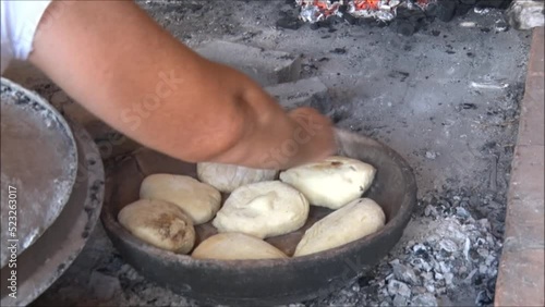 A woman bakes small loaves of bread in a special earthen pot that is heated on a charcoal grill