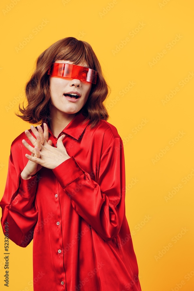 an attractive, sweet, thoughtful woman stands on a yellow background in a red shirt and fashionable glasses of an interesting shape, holding her fingers folded together near her chest an attractive, sweet, thoughtful woman stands on a yellow background in a red shirt and fashionable glasses of an interesting shape, holding her fingers folded together near her chest
