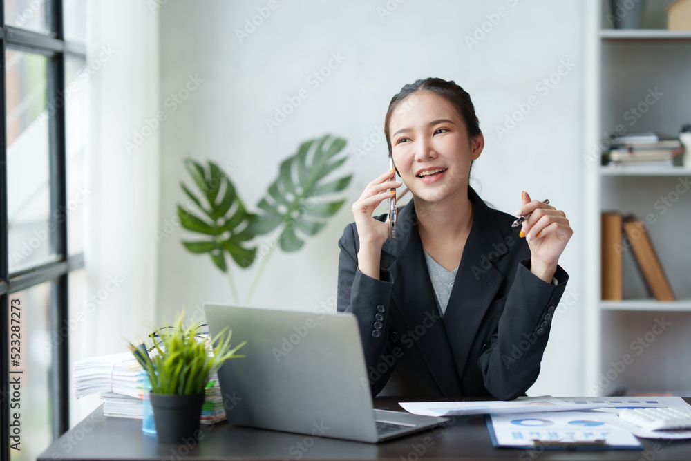 Beautiful Asian businesswoman using a smartphone to talk on the phone with a client in the office. smiling and happy at work. Beautiful Asian businesswoman using a smartphone to talk on the phone with a client in the office. smiling and happy at work.