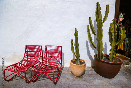 Vintage house exterior with two red chairs and clay pots with cacti against a white wall. Traditional Canarian decor