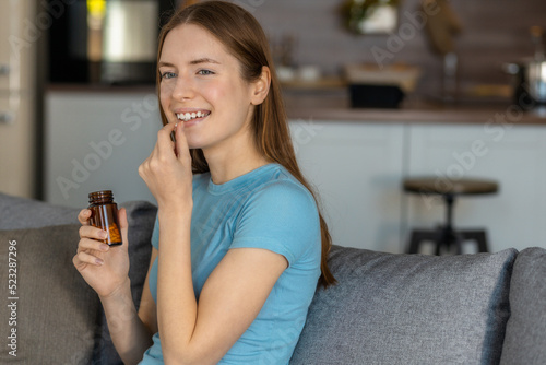 Happy smiling woman taking vitamin pill or painkiller capsule sitting on sofa at home