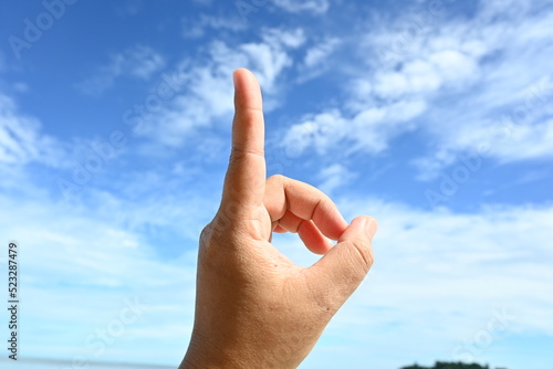 Woman pointing at something on blue sky background, closeup of hand and index finger